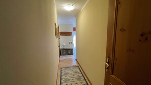 Un pasillo estrecho con un tapete estampado, una puerta de madera a la derecha y un accesorio de iluminación en el techo.