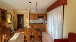 Un comedor con una mesa y sillas de madera, una cocina al fondo y un sofá rojo.