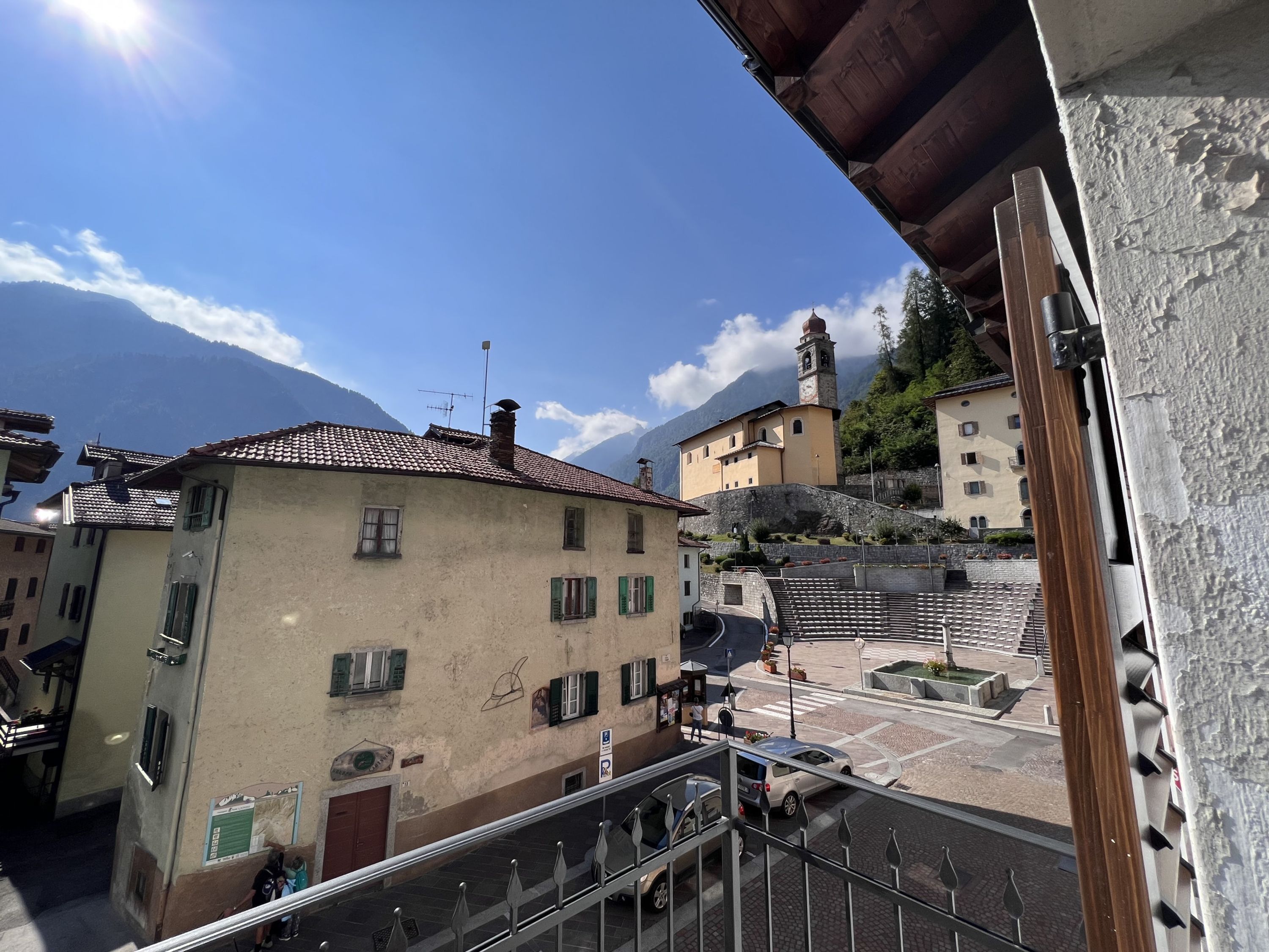 Un balcon donnant sur une place de ville, des bâtiments et des montagnes.