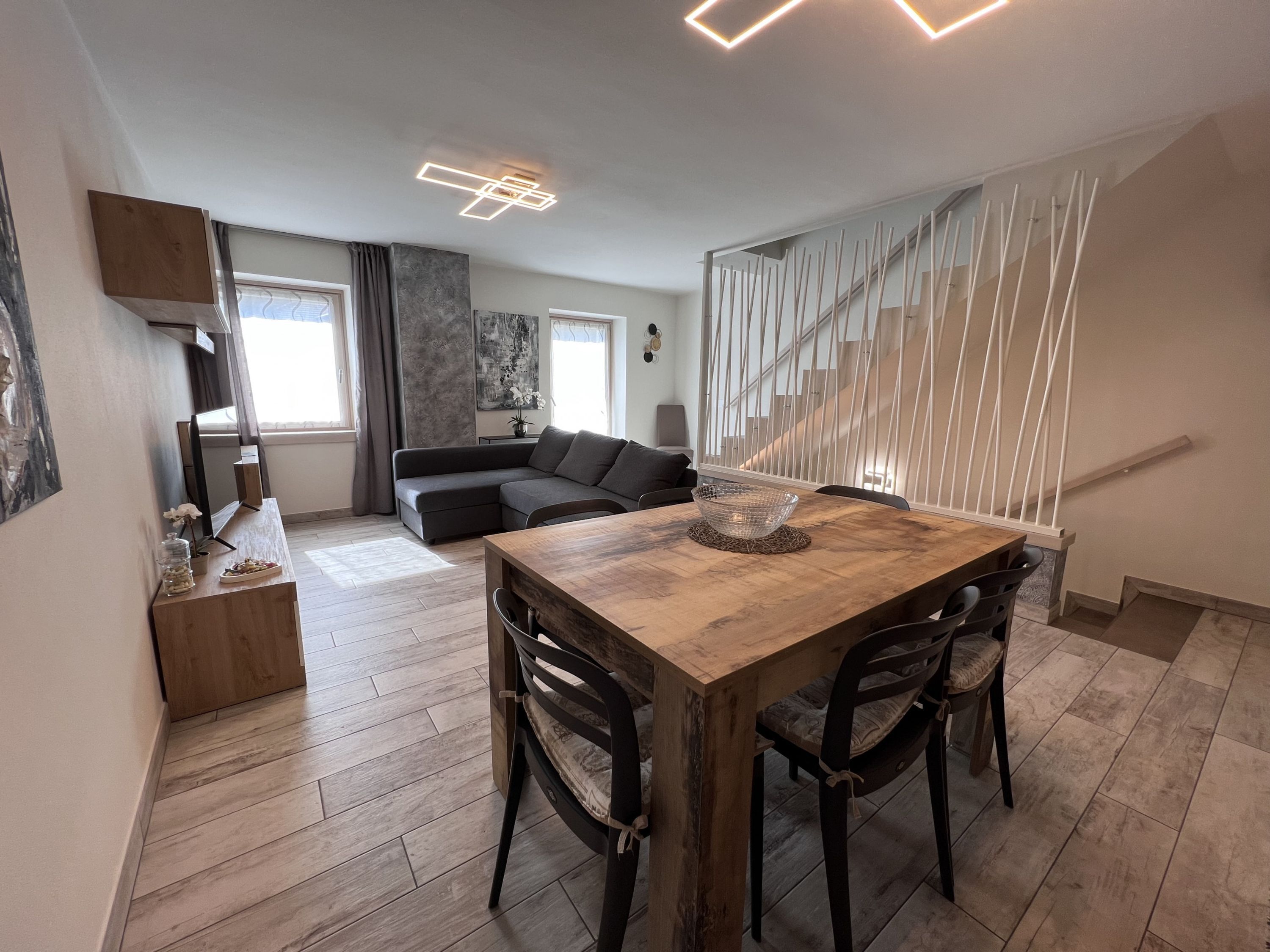 Ein moderner Wohnraum mit einem Holzesstisch, dunklen Sofas und einer Treppe mit weißen Geländern.