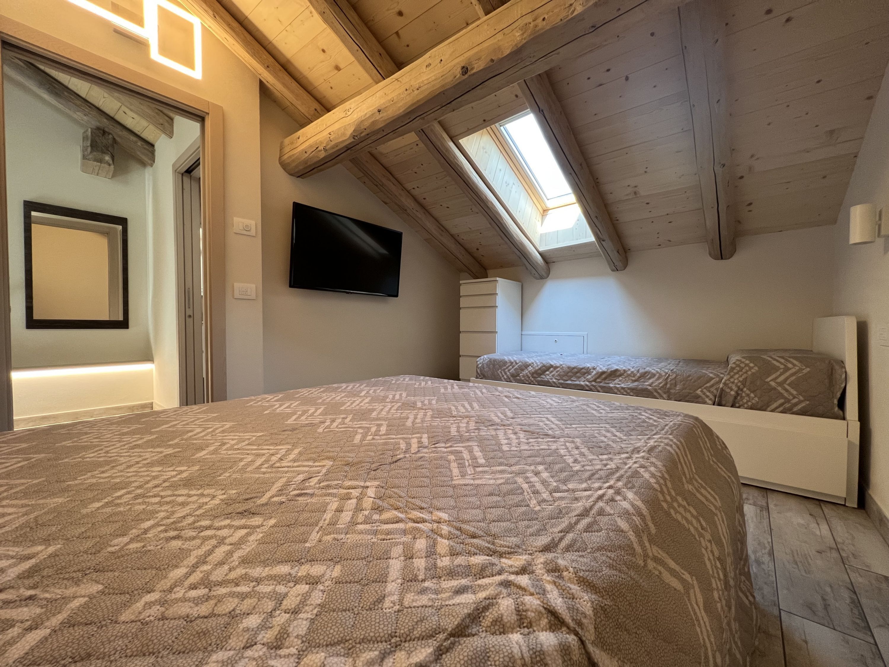 Une chambre avec un grand lit, un téléviseur fixé au mur et une lucarne.
