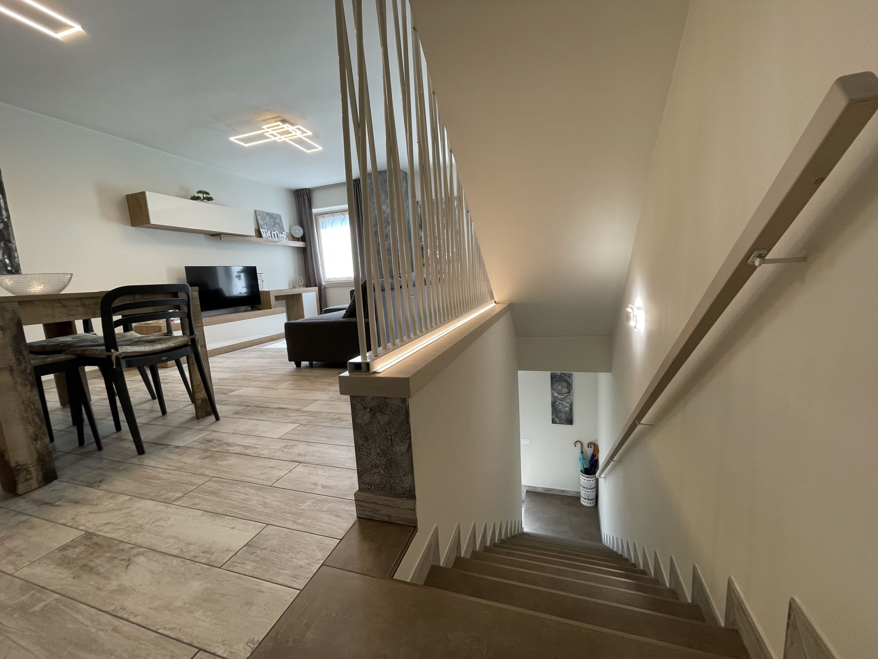 A staircase with a modern design, leading to a living area with a dining table and chairs.