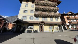 Un hotel a più piani con balconi, un ristorante al piano terra e montagne sullo sfondo.