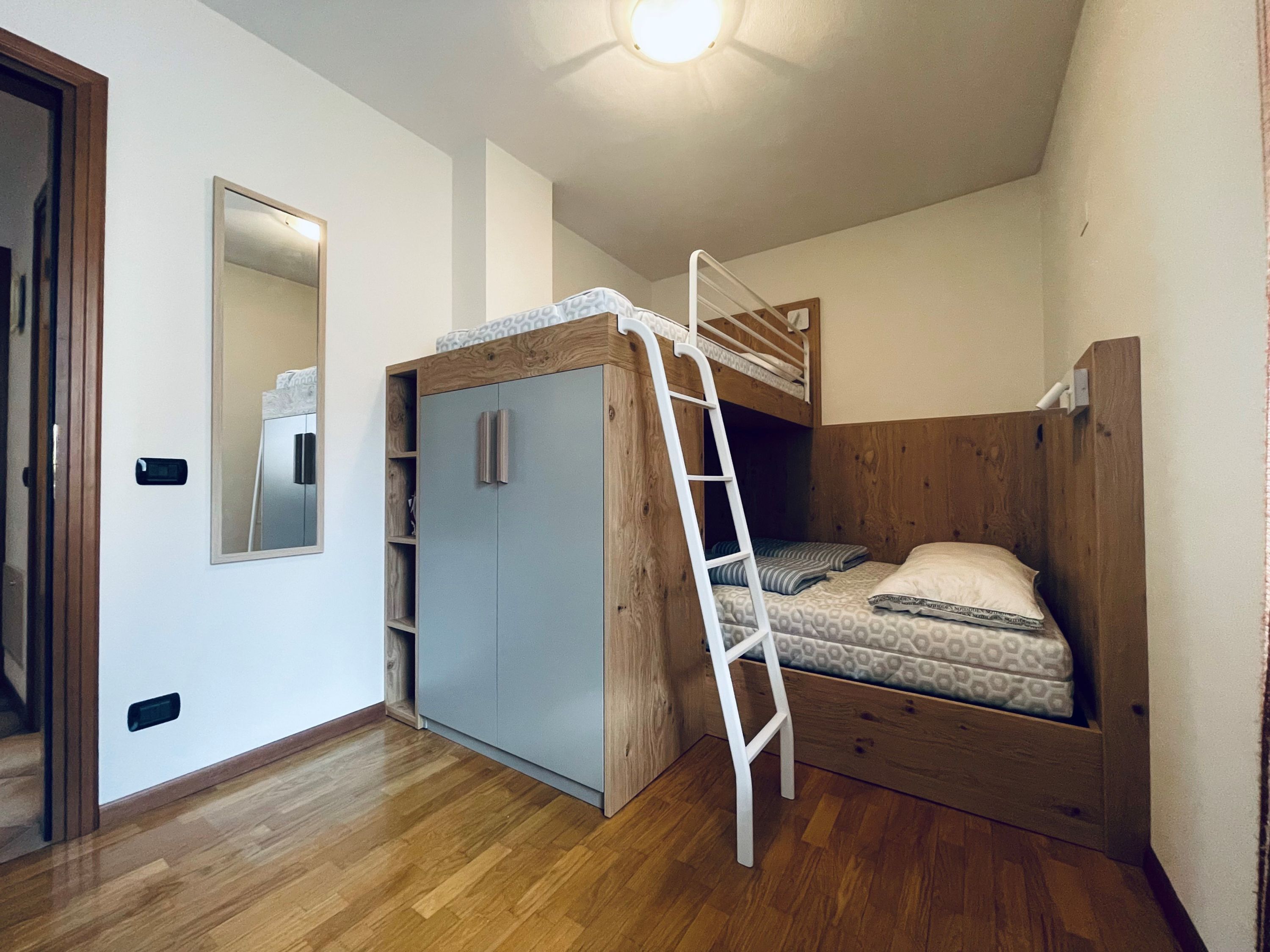 Une petite chambre comprenant un lit superposé, une armoire et un miroir.