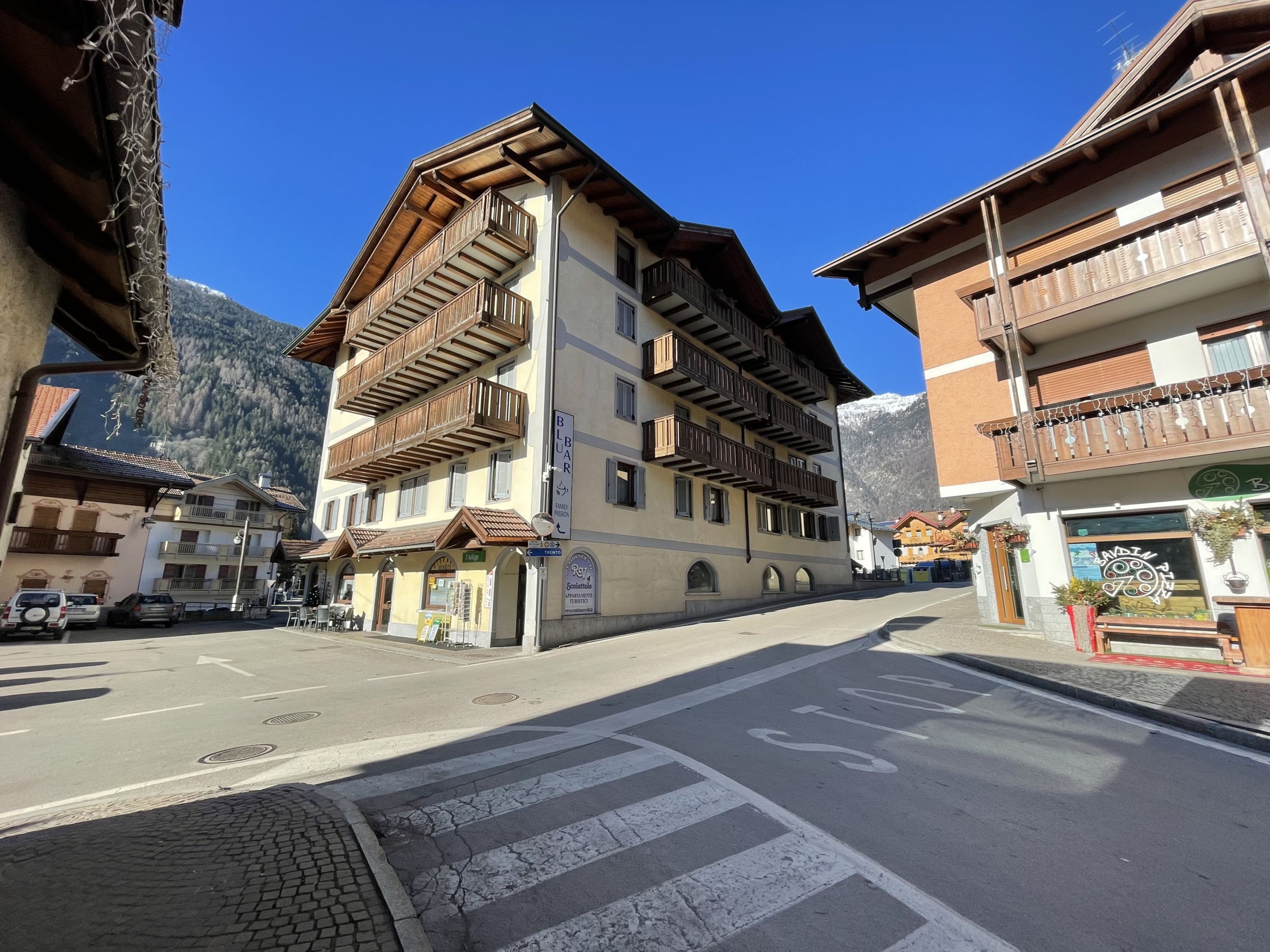 Une vue de rue présentant une architecture alpine traditionnelle, avec des bâtiments à plusieurs étages dotés de balcons en bois et un ciel d’un bleu éclatant.