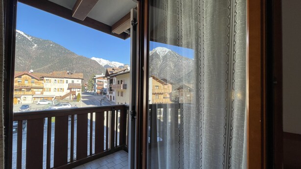 Un balcone con vista su una cittadina montana, ringhiere in legno e una tenda decorata.
