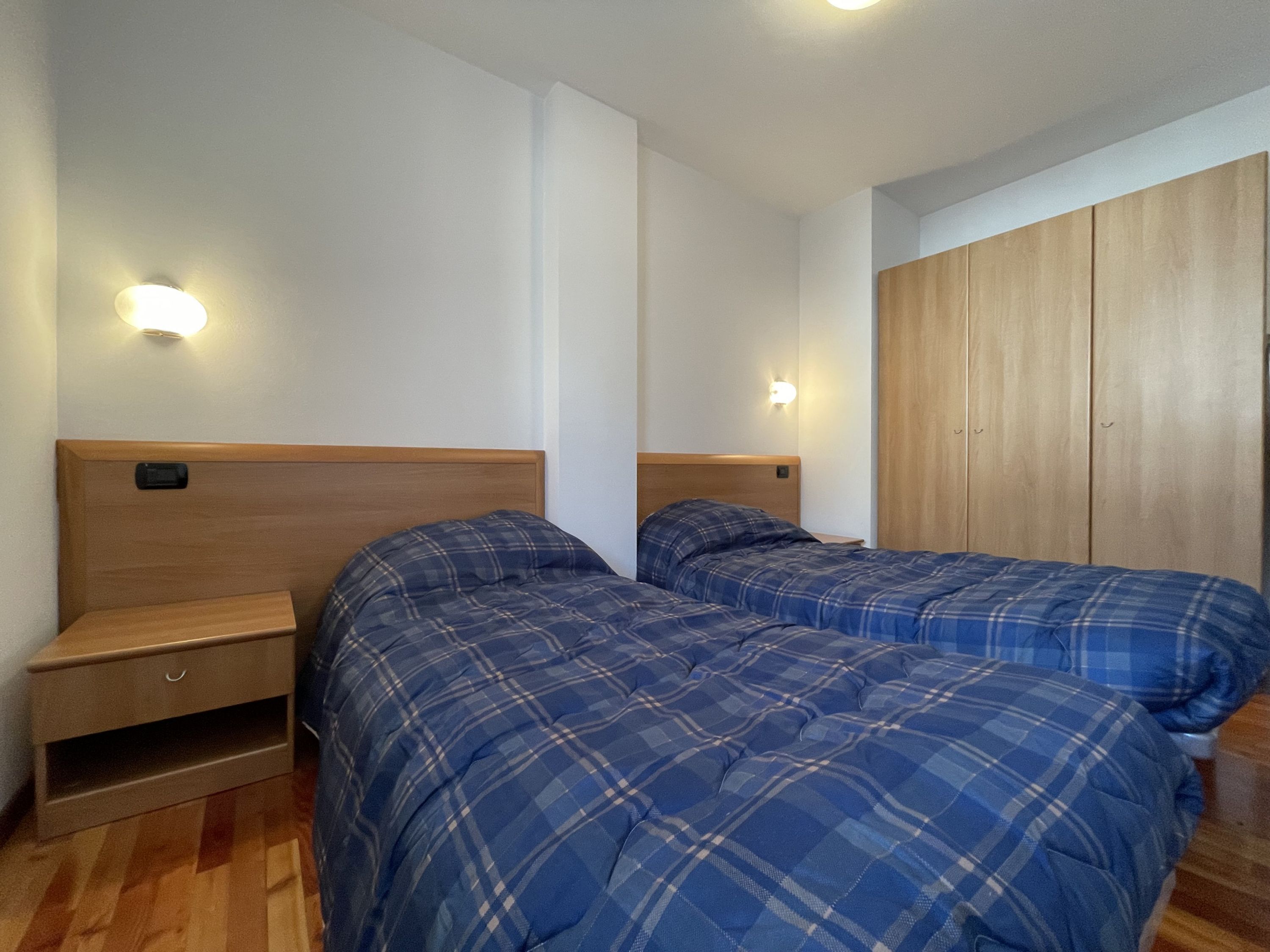 A bedroom with two beds, wooden headboards, bedside tables, and a wardrobe.