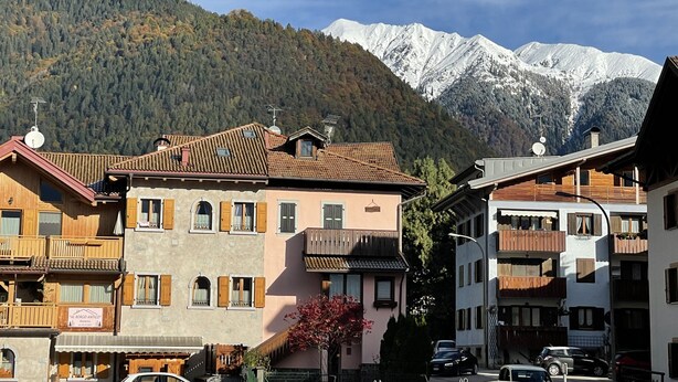 A mountain town with traditional wooden buildings, a sign for 'Al Borco Antico', and snow-capped mountains in the background.