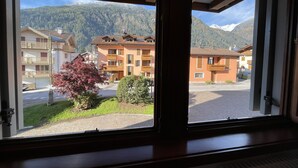 A window view of a building with balconies, a paved area, and a mountain backdrop.
