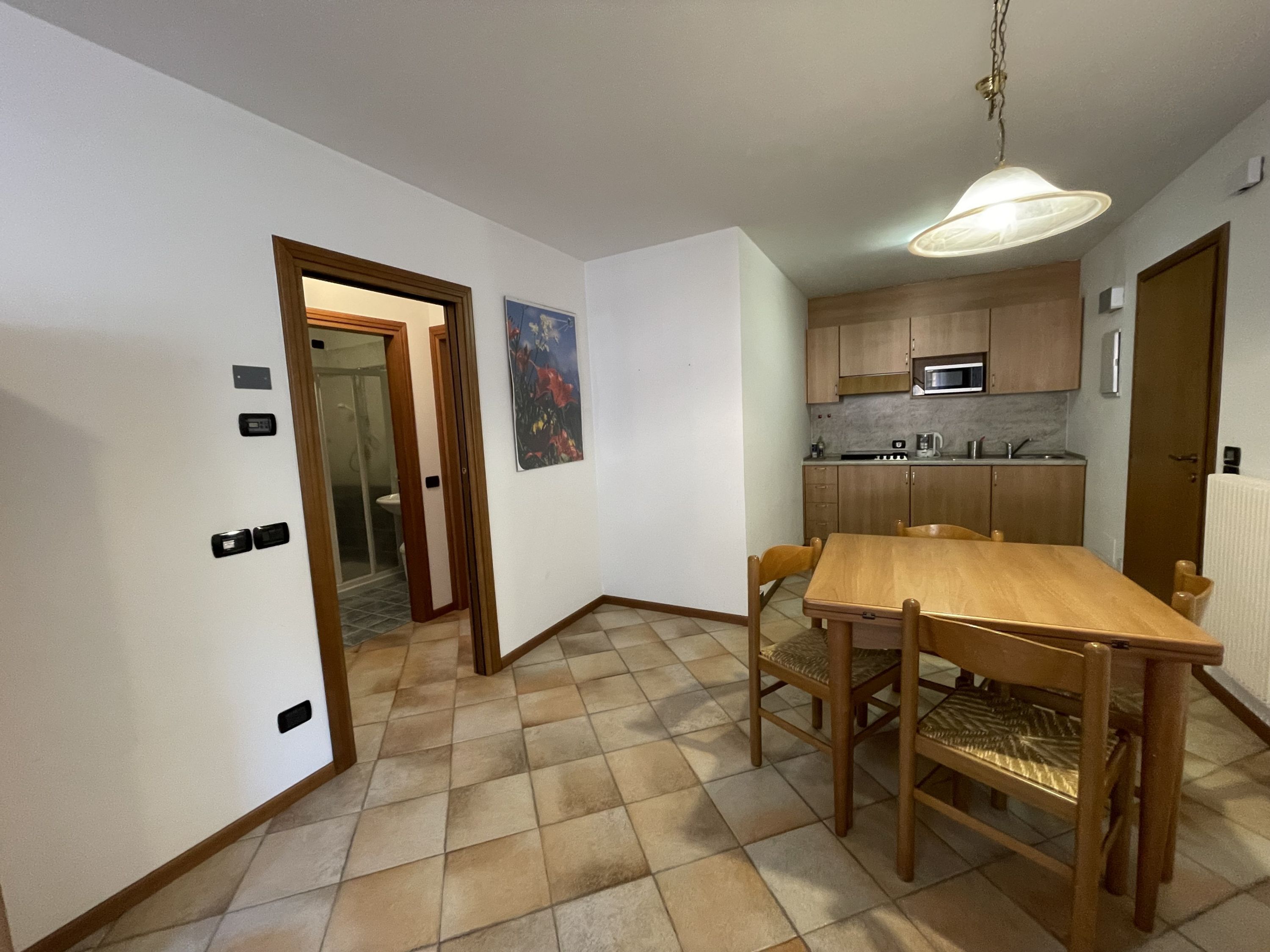 A compact kitchen with wooden cabinets, a microwave, and a dining area with a wooden table and chairs.