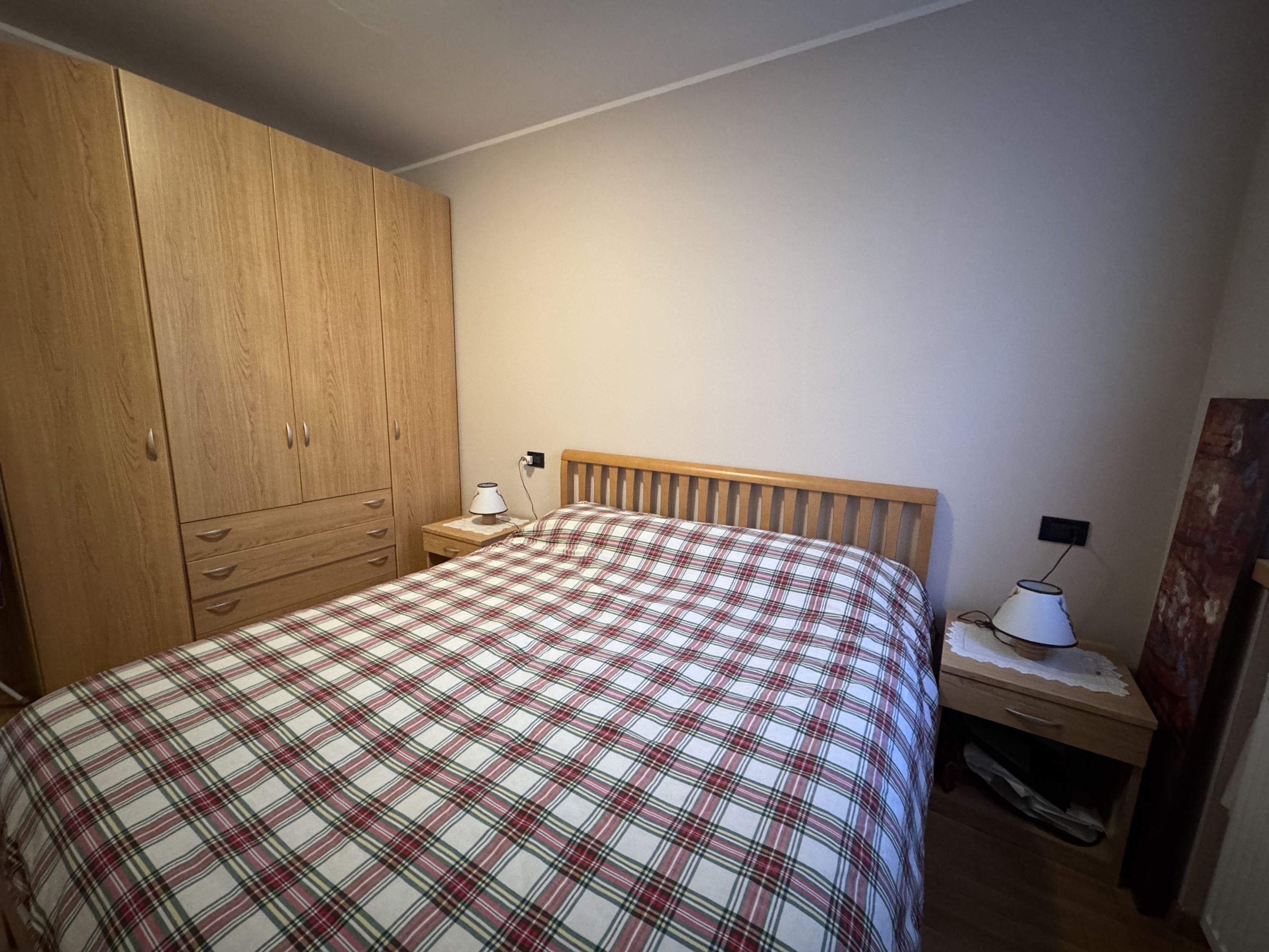 Un dormitorio con una cama, un armario de madera, una mesita de noche con lámpara y un escritorio con lámpara.