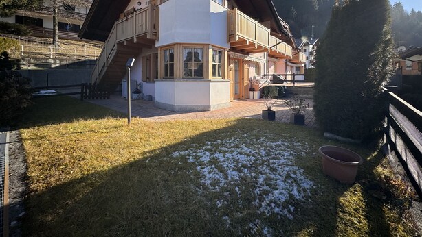 Een tweelaags huis met een balkon, een overdekte veranda en een kleine tuin met sneeuwvlekken.