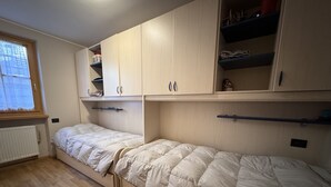 Een slaapkamer met twee bedden, houten kasten, een radiator en een raam.