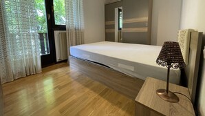 A bedroom with a wooden floor, a bed, a bedside table with a lamp, and a window with curtains. - 033 Trilocale Carisolo (Carisolo)
