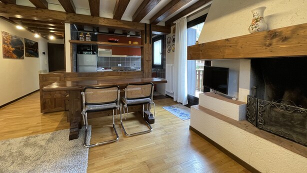 A modern kitchen with wooden beams, a central island, and a fireplace. - 033 Trilocale Carisolo (Carisolo)