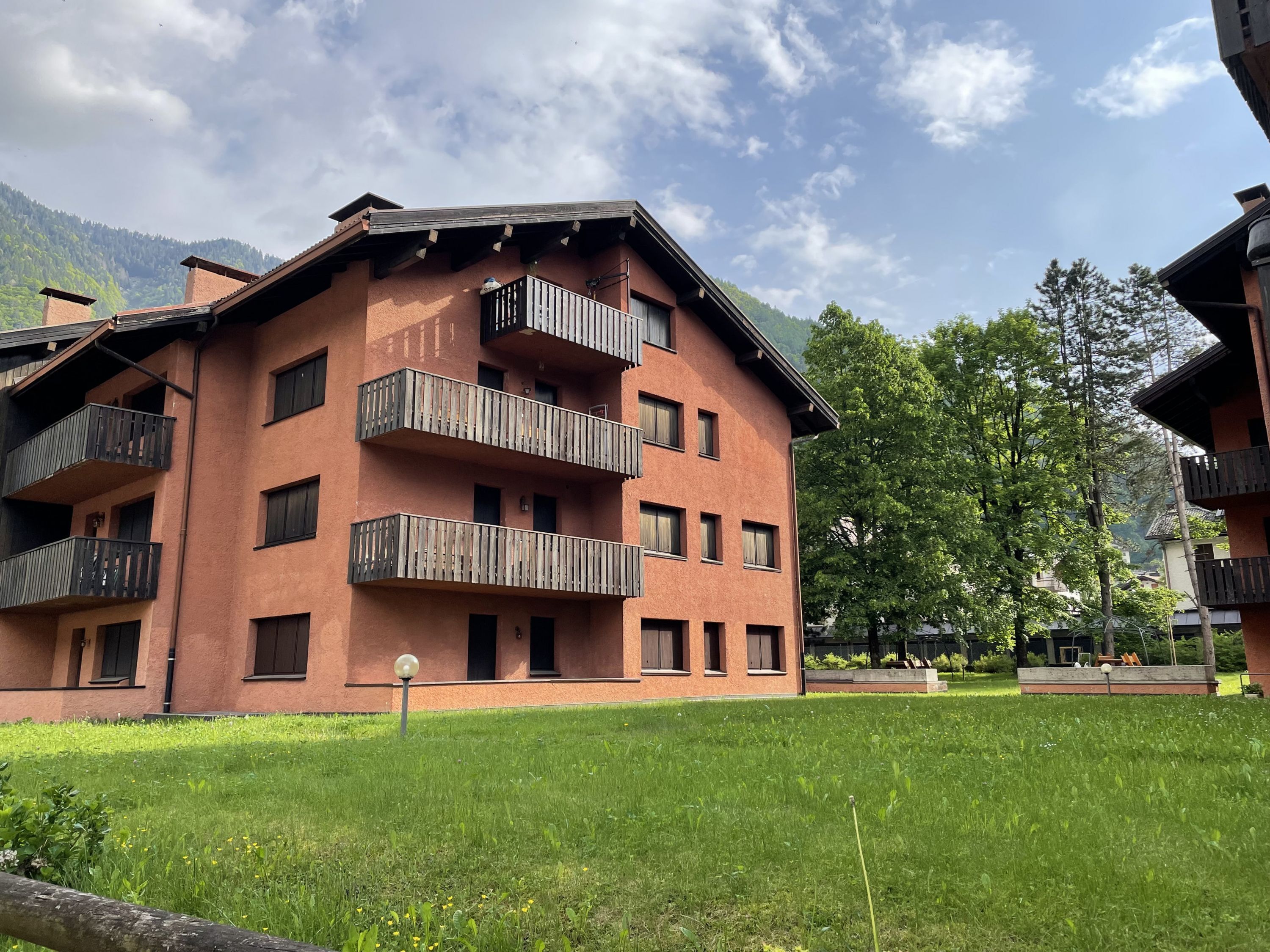 Un edificio de varios pisos con balcones, un patio con césped y montañas al fondo.