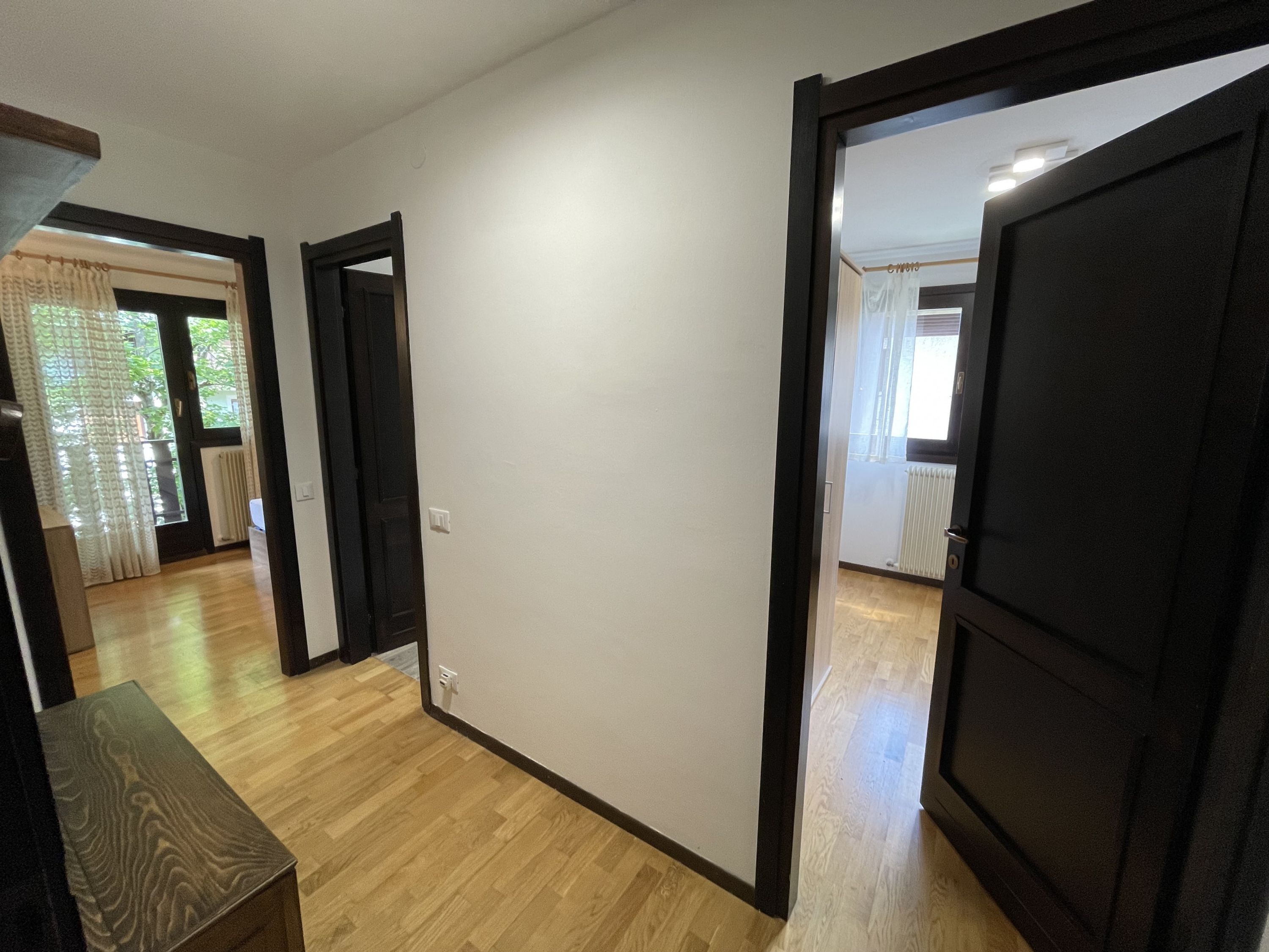 Un pasillo con suelo de madera, paredes blancas y puertas enmarcadas en negro que dan a otras habitaciones.