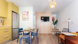 A compact living space with a kitchenette, a dining area with blue chairs, a sofa, and a TV mounted on the wall. - Sunset House (Málaga)