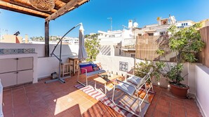 A rooftop terrace with a wooden pergola, a table with chairs, a potted plant, and a view of surrounding buildings. - Sunset House (Málaga)