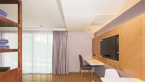 Une chambre d’hôtel moderne avec un plancher en bois, un téléviseur fixé au mur, un bureau et une chaise.