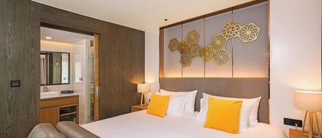 A modern hotel room with a large bed, wooden paneling, a decorative wall piece, and a bathroom with a mirror and sink.