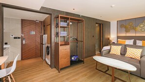 Une chambre d’hôtel moderne avec une armoire en bois, un canapé agrémenté de coussins à motifs, une planche de surf et un lave-linge encastré.
