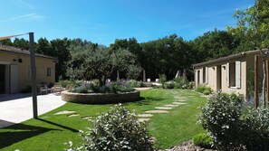 A courtyard with a stone circular planter, a lawn with stepping stones, and a building with a tiled roof. - Contemporary country house with a pool and air conditioning – Luberon. (Roussillon)