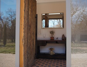 Une pièce avec une porte en bois, un miroir, une plante en pot, un vase et une petite table sur laquelle se trouve un verre à vin.