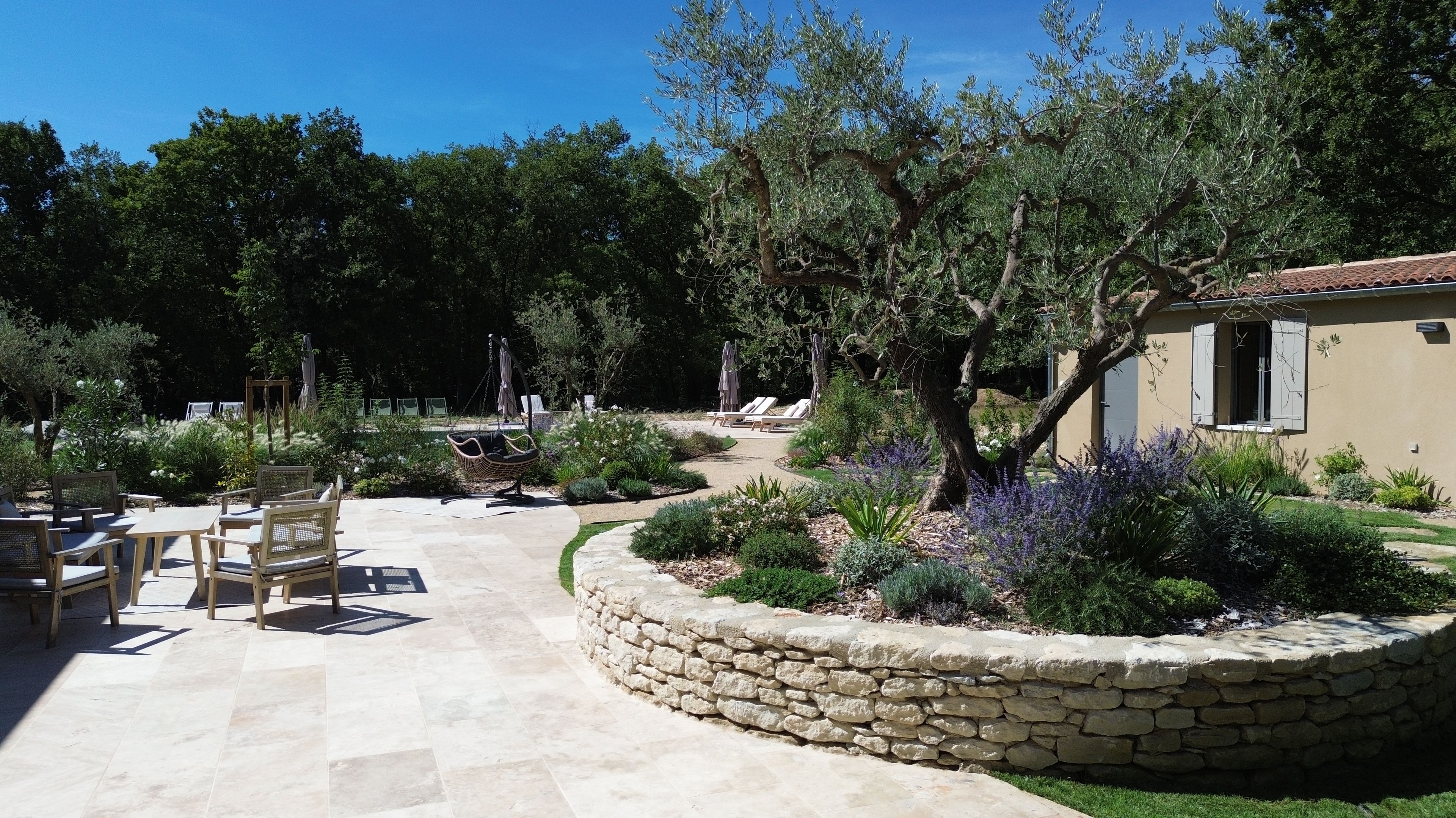 A patio area with stone flooring, outdoor seating, and a garden with various plants and trees.