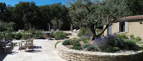 A patio area with stone flooring, outdoor seating, and a garden with various plants and trees.
