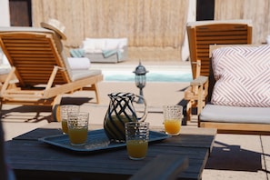 Un espace aménagé au bord de la piscine, avec des chaises longues, une table avec des boissons et un pichet décoratif.
