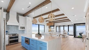 Een moderne keuken met blauwe kastjes, een groot eiland en uitzicht op zee.