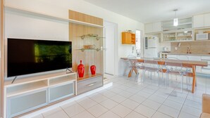 Una sala de estar moderna con un televisor de pantalla plana, pared revestida de madera y un comedor con mesa y sillas de madera.