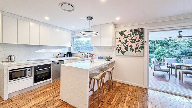 A modern kitchen with white cabinets, a central island, wooden flooring, and a view of greenery through a sliding glass door. - ☆☆☆☆☆ Spacious 4-bedrooms apartment in West Ryde (West Ryde)