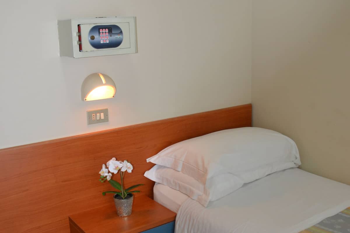 A hotel room with a bed, a nightstand with a lamp, and a thermostat on the wall.