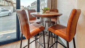 A modern dining area with a round table and four leather chairs, a potted plant on the table, and a view of the street outside. - 2 bedroom accommodation in Narbeth (Narbeth)