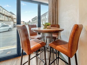 Un espace repas moderne avec une table ronde et quatre chaises en cuir, une plante en pot posée sur la table et une vue sur la rue.