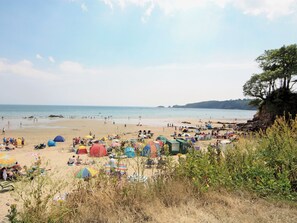 Une plage avec des tentes et des parasols, une plage de sable et une falaise bordée d’arbres.