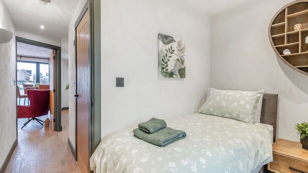 A bedroom with a bed, a bedside table, a wall-mounted shelf, and a door leading to a hallway. - 2 bedroom accommodation in Narbeth (Narbeth)