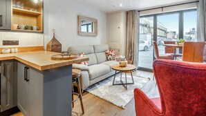 Um espaço de estar moderno com cozinha, um sofá, uma cadeira vermelha e vista para a rua.