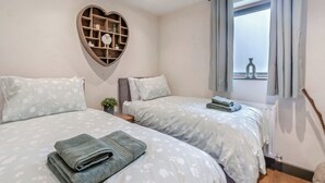 Quarto com duas camas, uma prateleira em formato de coração e uma janela com cortinas.