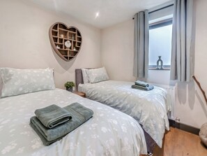 Une chambre avec deux lits, une étagère en forme de cœur et une fenêtre avec des rideaux.