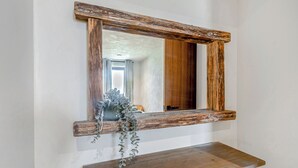 Uma prateleira de madeira rústica com um espelho acima, refletindo um quarto com porta e janela.