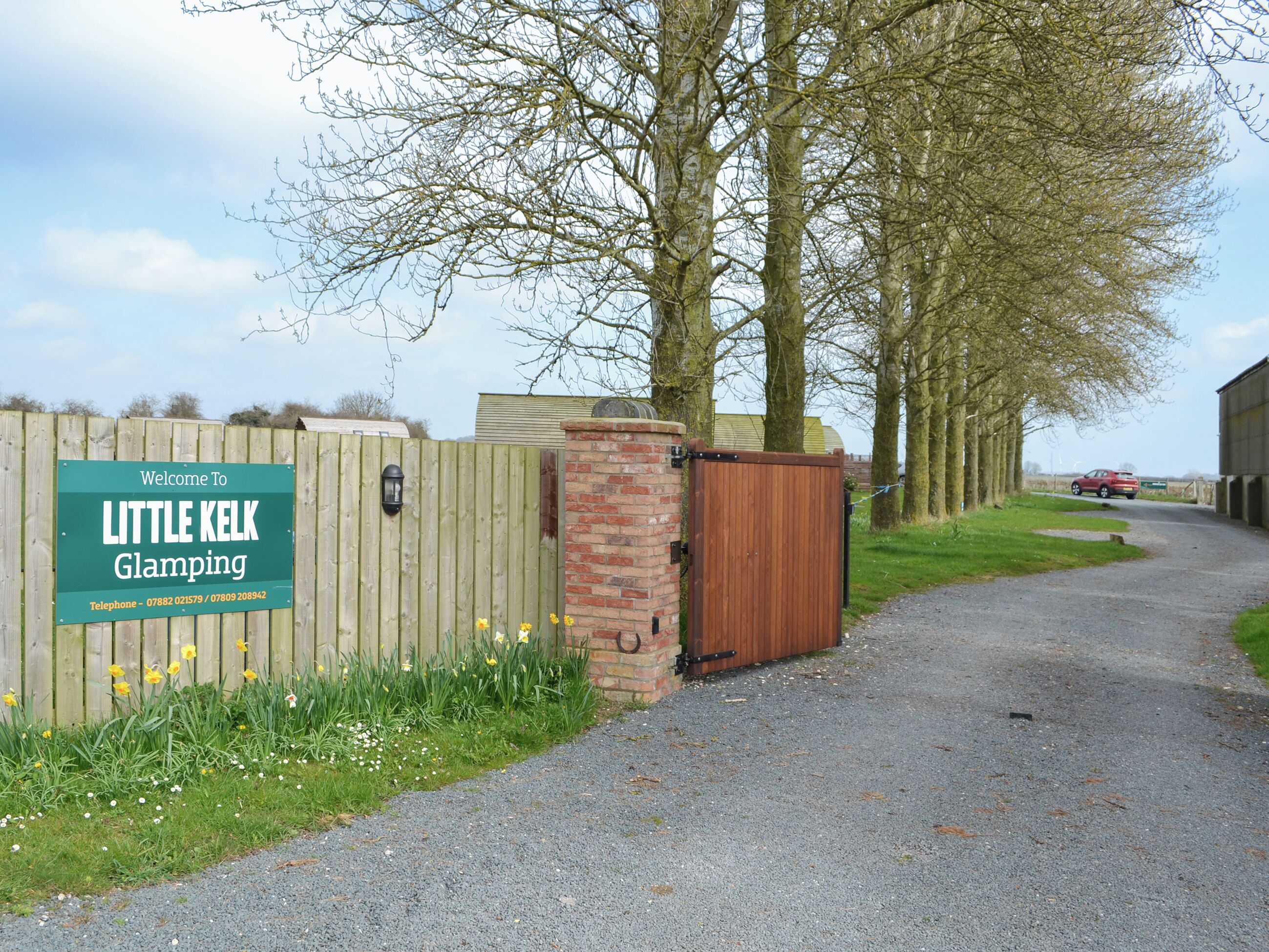 Een grindpad dat leidt naar een hek met een bord dat bezoekers verwelkomt bij Little Kelk Glamping.