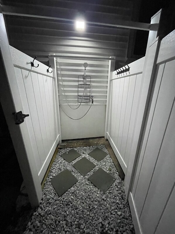 A small, enclosed space with a shower, a tiled floor, and a door with a handle.