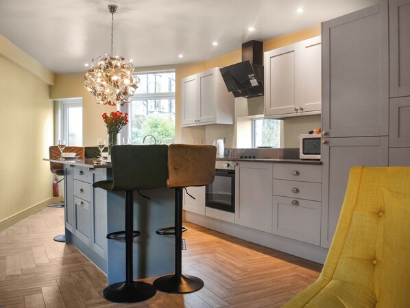 A modern kitchen with a central island, bar stools, a hanging light fixture, and a view of the outdoors.