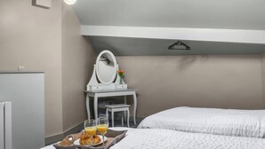 Une chambre d’hôtel avec deux lits, une coiffeuse avec un miroir et un plateau avec des croissants et du jus d’orange.