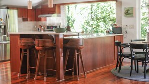A modern kitchen with a large island, wooden stools, and a dining area with a table and chairs. - Dreamy 5-bedroom Estate in Beautiful Downtown Nevada City with Pool (Nevada City)