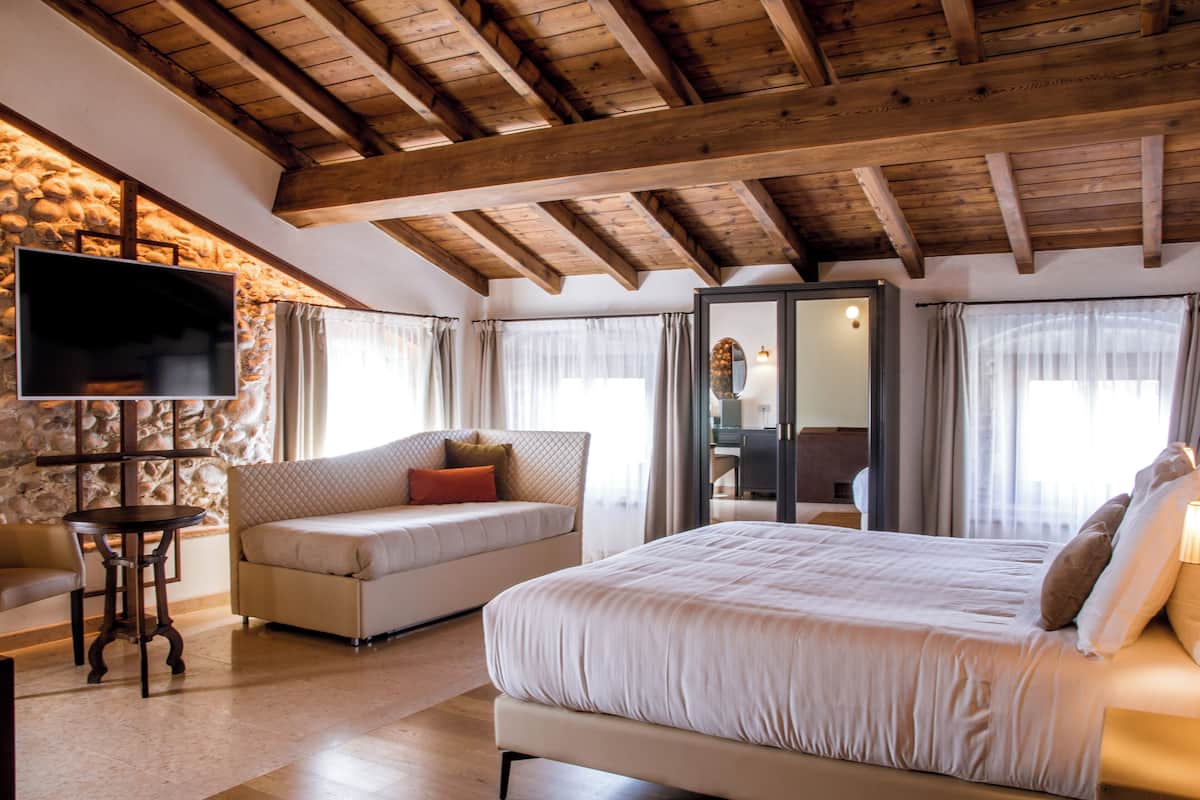 Une chambre avec un grand lit, un canapé, un téléviseur fixé au mur en pierre et un plafond en bois.