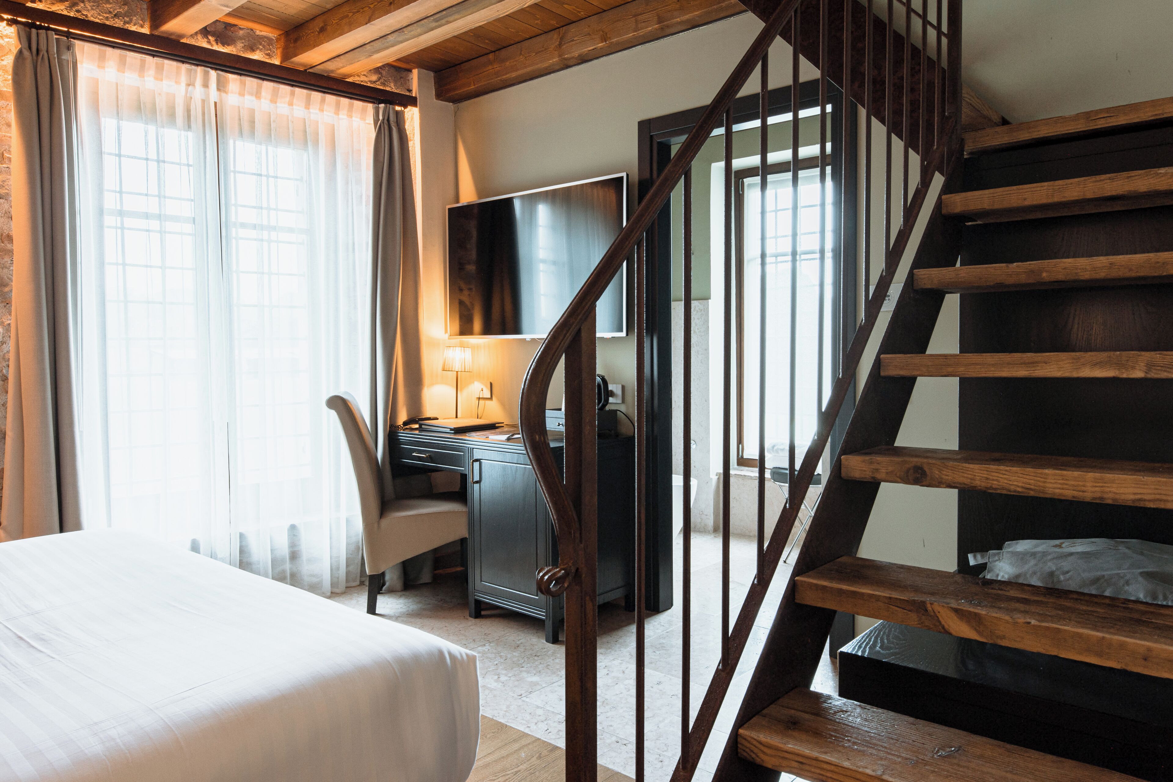 Habitació d'hotel amb llit, escriptori, cadira i escala de fusta.